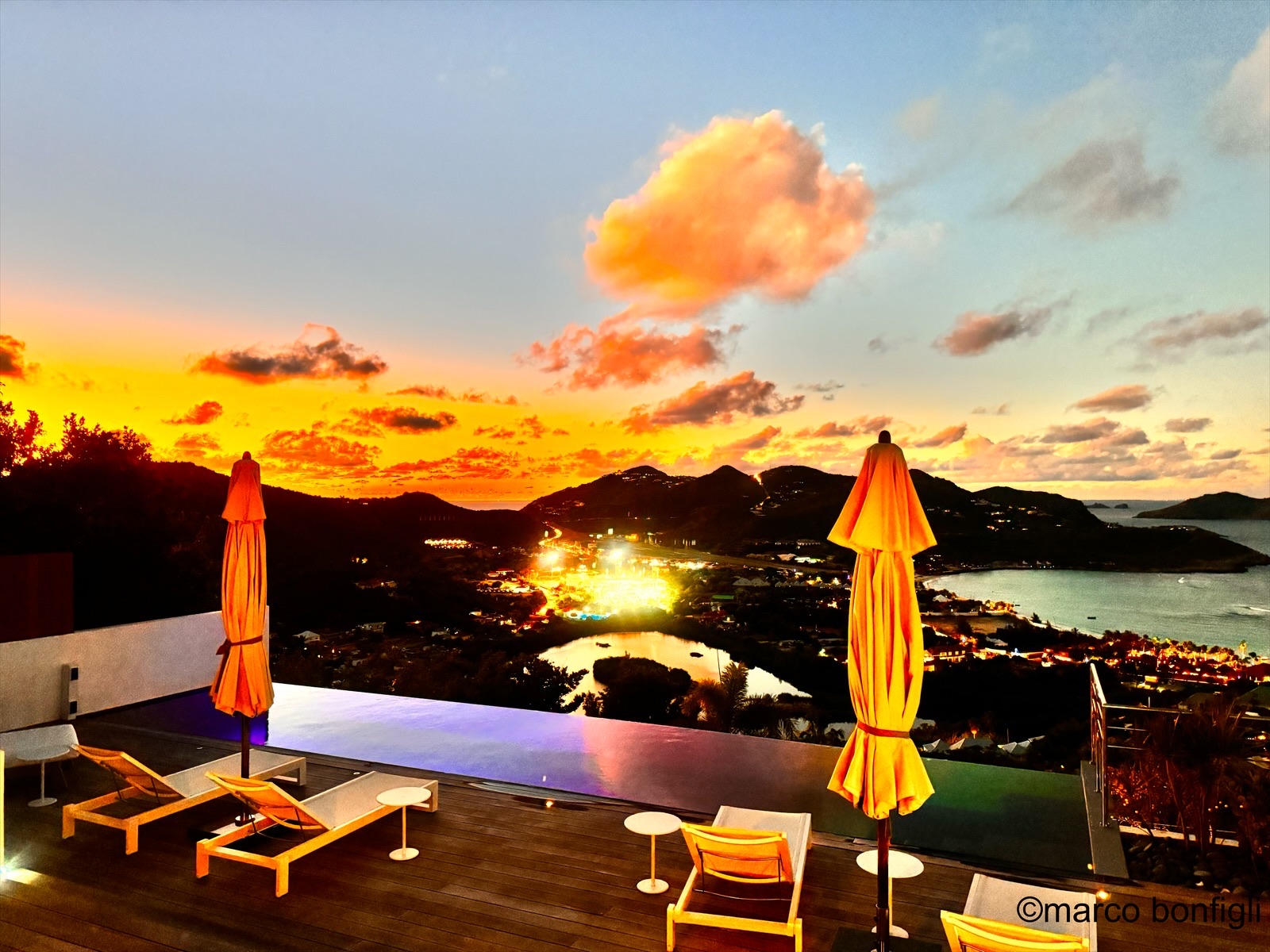 Infinity pool terrace at sunset with fiery skies over St. Jean and the lights of the island