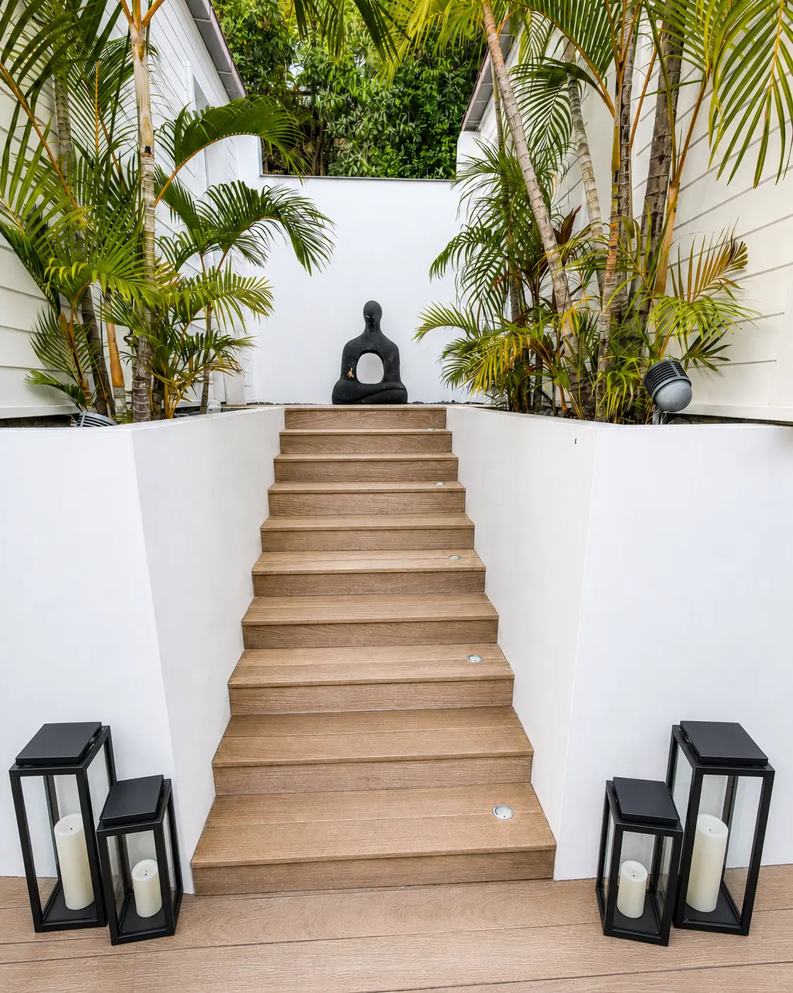 Timber stairs rising between white walls and palms to a seated statue