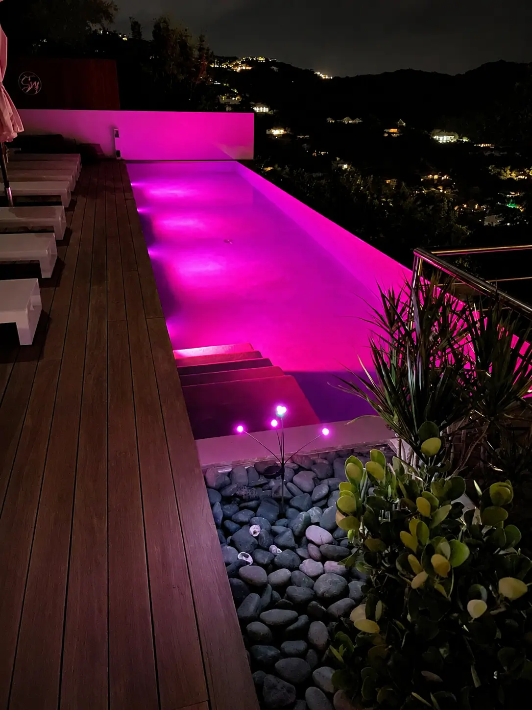 The infinity pool lit at night above the lights of the hillside