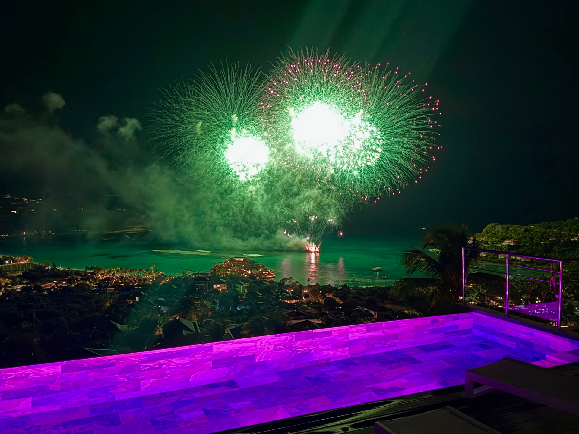 Fireworks bursting over St. Jean Bay seen from the magenta-lit infinity pool at night